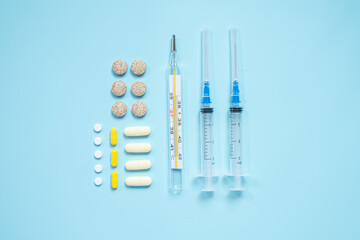 Medical supplies on blue background with pills, thermometer, and syringes