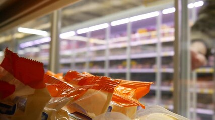 Close-up of many orange cheese packs in a supermarket fridge and a male consumer with a shopping trolley takes one