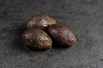 wet whole black avocado fruits of small size on a black slate