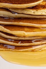 drizzled with honey, a large number of delicious pancakes stacked together on a white bowl, a tower of small milk pancakes with natural bee honey, close up