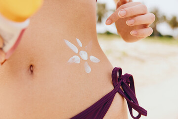 Woman in bikini holding sunscreen bottle on body standing on beach with flower painted on stomach