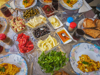 Turkish breakfast table. Flat-lay of peoples hands taking pastries, vegetables, greens, olives, cheeses, fried eggs, spices, jams, honey, tea in copper pot and tulip glasses, wide composition