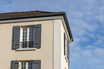 A sunny morning in the French town - a building's corner and French window with opened shutters, blue sky at the background