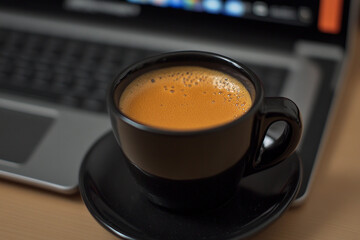 Close-up of a steaming coffee cup beside a laptop on a wooden desk during morning hours
