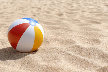 Obraz premium Colorful beach ball resting on warm sandy shore under a bright sun during a sunny summer day