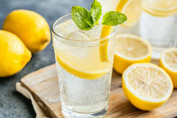 Refreshing glass of lemonade with mint and lemon slices on a wooden board in bright natural light