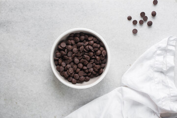 Overhead view of dark chocolate chips in a white bowl, top view of chocolate chips on a white background