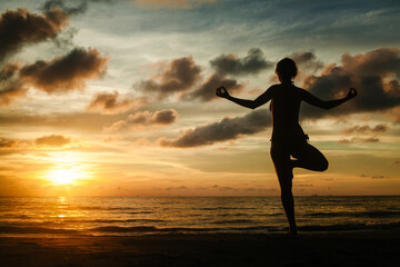 The silhouette of a woman practicing yoga on a tropical beach during a magical sunset.