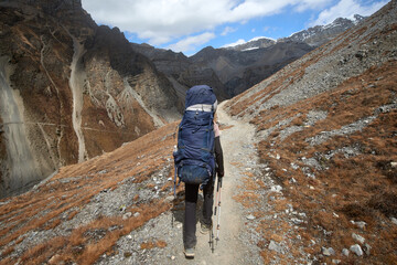 Traveler with backpack walks along mountain path alone enjoying an outdoor activity in Himalayas, Nepal.