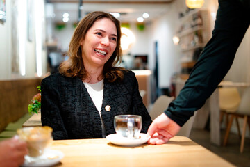 Smiling businesswoman having coffee break in cafe, waiter serving tea