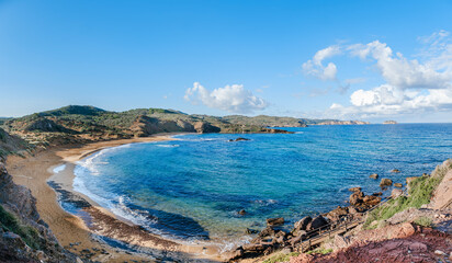 Captivating aerial view of Cala Cavalleria, Menorca, where turquoise waters gently kiss the unique reddish shores, offering a serene and secluded escape in Minorca, Spain