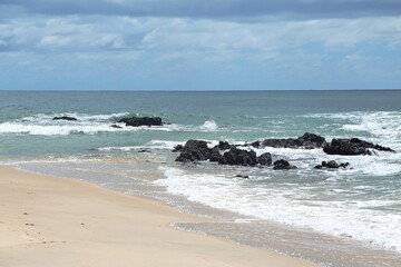 Blue sea water in Coqueiros beach, close to Joao Pessoa city, Paraiba, Brazil. Open wide ocean with waves crashing on reefs rocks at water edge, beach sand.
