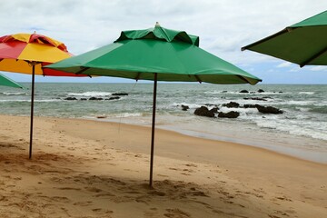 Vacations on tropical beach. Green parasol on the empty beach sand waiting for tourists, waves breaking on waters edge, splash and white foam. Coqueiros beach, near Joao Pessoa city, Brazil