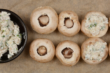 Six mushrooms stuffed with a creamy filling and a bowl of the filling, shot from above on baking paper