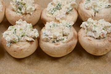 Six mushrooms stuffed with a creamy filling, arranged in two rows on baking paper, shot from above