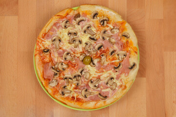 Pizza with ham, mushrooms, and an olive on a green plate, shot from above on a wooden surface