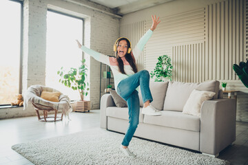 Obraz premium Young girl enjoying music indoors wearing headphones, dancing happily in a stylish living room with a modern interior on a bright daylight.
