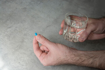 A man's hand holding a capsule and a glass of water