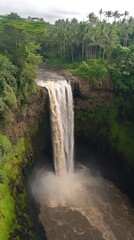 Obraz premium Aerial shot displays a tropical waterfall dropping through lush jungle greenery. Vertical.