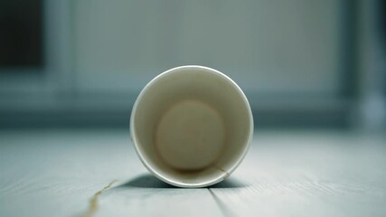An empty coffee cup fell on the floor.
A takeaway coffee cup fell on the floor.
A puddle and splashes of coffee on the wooden floor in the room.
Dirty floor