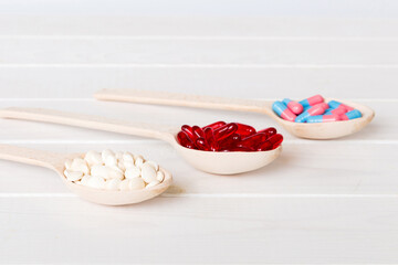 Vitamin capsules in a spoon on a colored background. Pills served as a healthy meal. Red soft gel vitamin supplement capsules on spoon