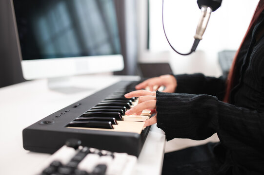 Beautiful Asian teen girl playing guitar, composing music in home recording studio using computer, headphones, condenser microphone, tablet and keyboard for mixing and mastering music. - Powered by Adobe