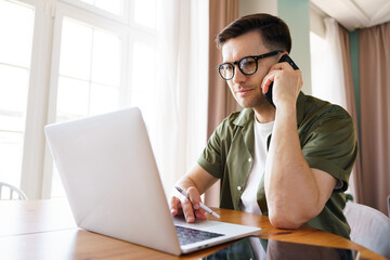 Fototapeta premium Young Professional Engaged in Remote Work While Communicating Over the Phone in a Cozy Workspace