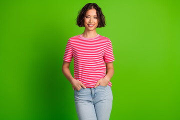 Young multiethnic woman smiling confidently in casual striped t-shirt against green background,...