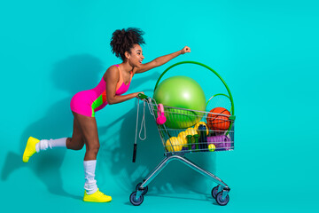 Fototapeta premium Young woman pushing a cart filled with fitness gear in vibrant and colorful sportswear, expressing a dynamic and active lifestyle.