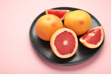 Whole grapefruit with slice on dark plate on pink background.