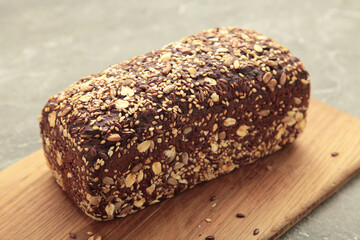 Wheat bread with mixed seeds on cutting board on grey background