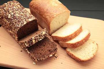 Different bread on cutting board on dark wooden background.