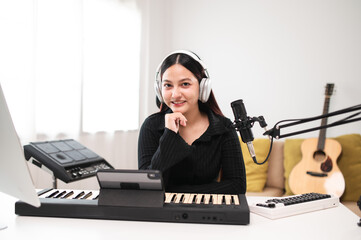 Beautiful Asian teen girl playing guitar, composing music in home recording studio using computer,...