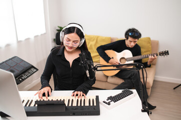 Asian teenagers, men and women playing guitar, composing music in home recording studio using...