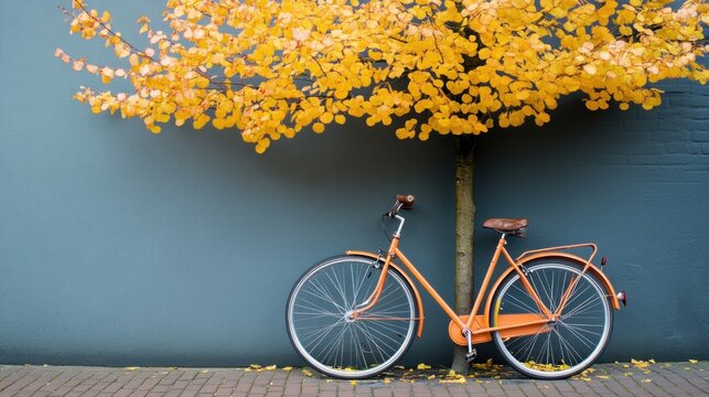 Vintage bicycle resting against a blue wall under a tree with yellow leaves
