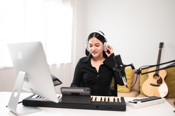 Beautiful Asian teen girl playing guitar, composing music in home recording studio using computer,...