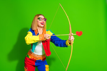 Colorful woman with glasses holding a wooden bow and heart arrow on green background in vibrant and...