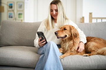 Portrait of a young woman on the livingroom with golden retriever dog using cellphone