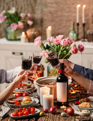 Group of happy friends clinging glasses of wine. Easter holiday table with wine, color eggs, baked meat with vegetables, candles, flowers for festive dinner at home. Celebration concept, toning