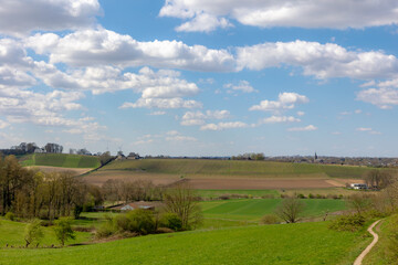 Fototapeta premium Overview of Maastricht, Terrain of hilly countryside green grass meadow and farmland, Combination with old and new modern buildings, Houses and church on hillside with blue sky, Limburg, Netherlands.