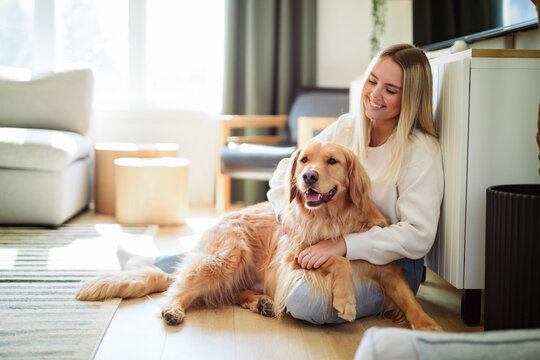 Portrait of a young woman on the livingroom with golden retriever dog indoors at home.
