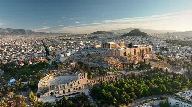 Fly around Parthenon in Athens - famous Greek tourist attraction. Aerial view of Parthenon in Athens, Greece at sunrise. Acropolis is illuminated with city lights, ancient theater sitting below