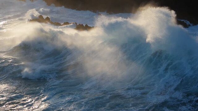 Huge power ocean wave crashing over sunset sky background. Slow motion of stormy ocean surf splashing on the coast of Madeira, Porto Moniz