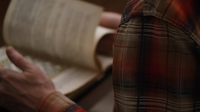 blurry man is studying chess textbook. person flips through pages illustrated book to study chess game. visual aid. view over his shoulder. hobby.