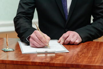young man standing at wedding ceremony and signing wedding documents, groom in black costume, cropped, unrecognizable