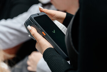 waitress holding in hands electronic cash register for contactless payment with paper receipt in cafe or restaurant, smart terminal, green check mark of payment confirmation on display, close-up view