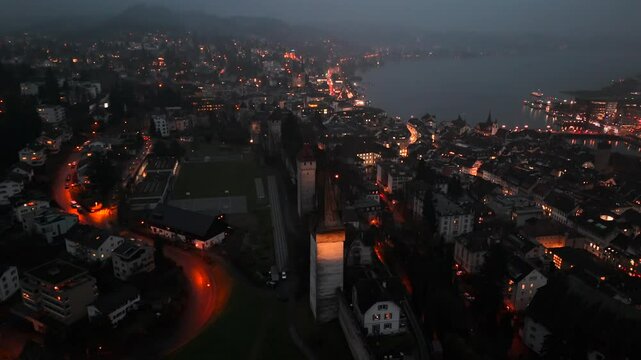 Musegg Wall and its nine towers aerial view at night overlooking glowing city in Lucerne, Switzerland. Medieval defenses of Lucerne. Museggmauer Luzern und ihre neun Tuerme Luftaufnahme bei Nacht. 