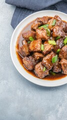 A delectable plate of Chinese stir-fried pork liver cubes in a rich, glossy brown sauce is garnished with vibrant green scallions offe a savory and flavorful culinary