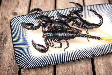 Roasted insects. Amazing exotic snack street food. Three fried Scorpions - Heterometrus laoticus on skewers ready to eat in ceramic plate on old wooden table.