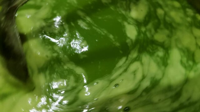 a close-up scene of green liquid foodstuffs being stirred with a spoon in a stainless steel container. 